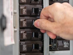 electrician turning on a switch in circuit breaker box